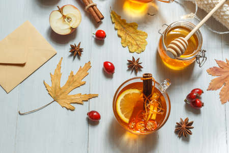 Autumn layout with fragrant hot tea, dry leaves, an envelope and a honey in a jar. On a light wooden...