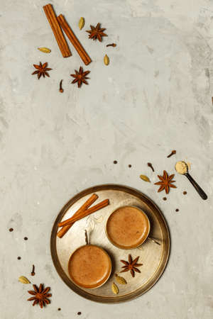 Hot fragrant masala tea in small copper cups on a round tray.On a grey stone background with spices, top view with spaceの写真素材