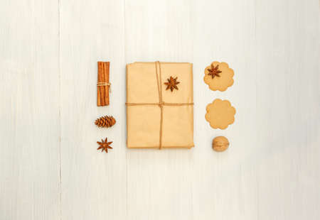 Flat lay in a warm color scheme with a gift in craft paper, cookies and spices on a light wooden...