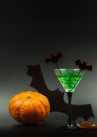 Halloween cocktail, green with bats. Close-up with space. Orange pumpkin and bat in the backgroundの写真素材