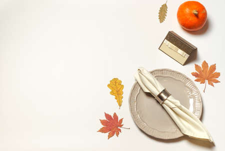 A ringed napkin on a gray plate and an empty name card on a white table with a small orange pumpkin and bright autumn leavesの写真素材
