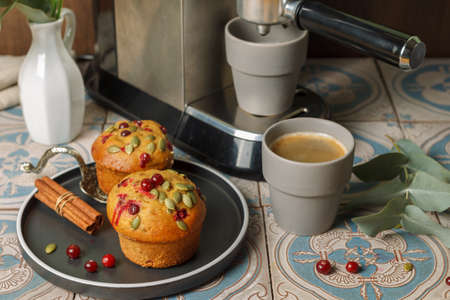 Two muffins with berries and seeds on a black plate and a coffee machine pouring espresso into gray cups.の写真素材