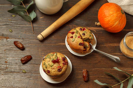 Two pumpkin muffins with cranberries and dates on a dark wooden table with baking ingredients. Top view with spaceの写真素材
