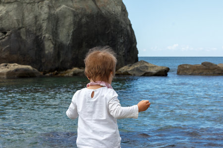 A kid with short blond hair walking to the sea. Holidays with children at a seaside resortの写真素材