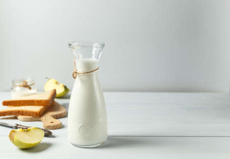 Milk or drinking yogurt, buttermilk in a glass bottle. On a light wooden table with croutons and an apple. Healthy breakfast with natural productsの写真素材