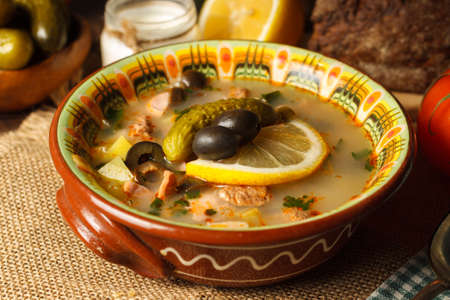 Meat solyanka, thick soup with different varieties of meat, sausages and smoked meats. In a painted ceramic bowl with olives, lemon and picklesの写真素材