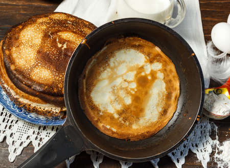 A pancake in a frying pan and a stack of pancakes in the background. Close-up. Traditional food for Maslenitsaの写真素材