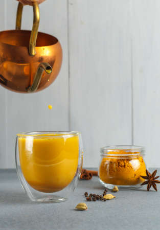 Golden moon milk with turmeric in a thermo glass. Pours from a vintage copper teapot, small drops. Vertical frame, selective focus. Hot Ayurvedic drinkの写真素材