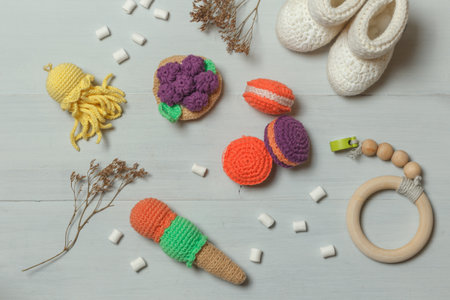Knitted amigurumi toys, ice cream, macaroons, baby booties and a wooden rattle. Layout on a gray wooden background. Eco-friendly toys for childrenの写真素材