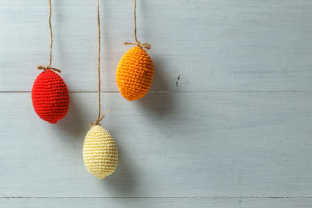 Home decor for Easter. Bright knitted Easter eggs hanging on strings. On a gray wooden background,...