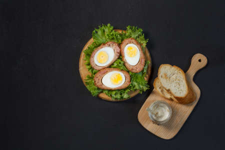 Scotch eggs, a hearty dish of British cuisine. boiled eggs are coated with minced ham and anchovies and fried in breadcrumbs until golden brown. Top view on a black background, with spaceの写真素材