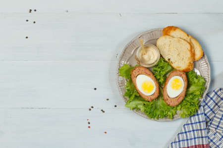 Scottish eggs, classic British appetizer, nutritious breakfast. On a plate with lettuce leaves and sauce. Top view on a gray wooden background, with spaceの写真素材