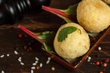 Arancini, a traditional Italian appetizer, fried rice balls with mozzarella. Close-up on a dark...