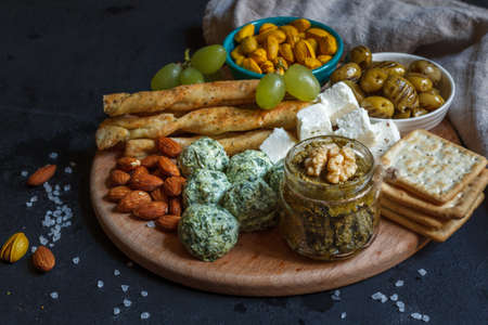 A set of snacks for a holiday, a party on a round wooden board. On a black background, close-up.の写真素材