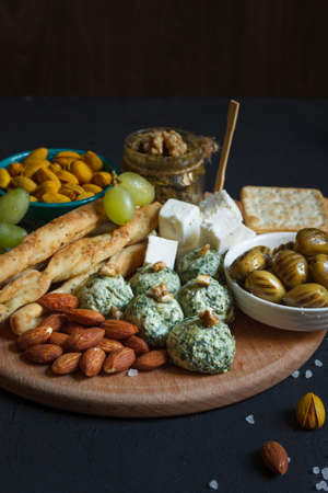 A set of snacks for wine, beer. Cheese, dried olives, spinach balls and cream cheese. Breadsticks and crackers. On a dark background, verticallyの写真素材