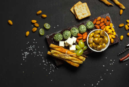 A set of snacks for wine, beer on a marble tray. Cheese balls with herbs, fried olives, bread sticks. Overhead, on a black background, with spaceの写真素材