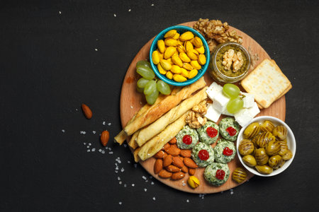 Assorted snacks for wine or beer on a wooden round tray. On a black background, overhead, a copy of the spaceの写真素材