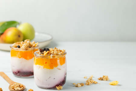 Two cups of healthy homemade yogurt with fruit and granola. Close-up, on a light background, copy of the spaceの写真素材