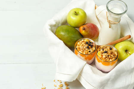 A wooden tray with fruit, a jug of milk and homemade yogurt with granola. On a light wooden background, horizontally with spaceの写真素材