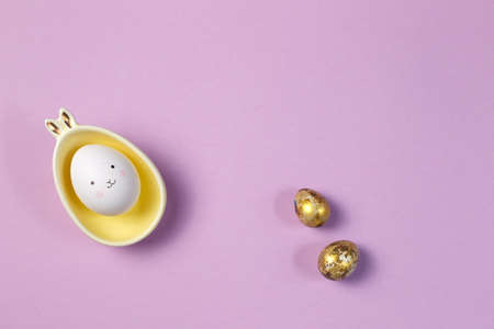 Easter content. A mockup on a purple background, an egg with a painted face in a stand with bunny ears, and painted eggs.の写真素材
