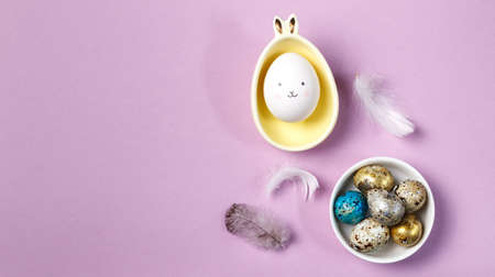 Easter content. A mockup on a purple background, an egg with a painted face in a stand with bunny ears, and painted eggs in a bowl.の写真素材