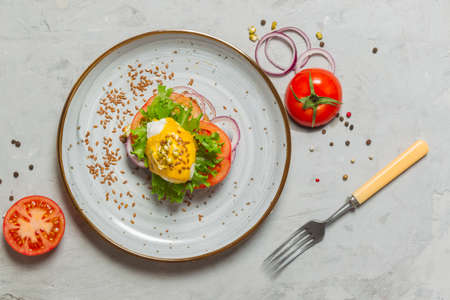 Breakfast with egg benedict. Poached egg sandwich with hollandaise sauce with tomato slices and red...