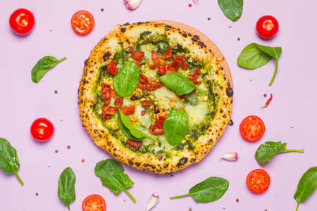 Healthy vegetarian pizza with pesto sauce, spinach, sun-dried tomatoes and pine nuts. Close-up, with cooking ingredients, top view, full frame, lilac paper backgroundの写真素材