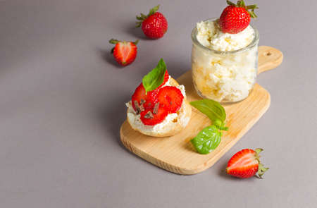 The concept of a delicious and healthy snack. Sandwich with ricotta, fresh strawberries, basil and grated chocolate. Close-up on a wooden board with a can of cheese and berriesの写真素材