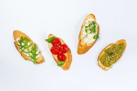 Bruschetta, a very tasty snack of fried bread slices, is one of the symbols of gastronomic Italy. With tomatoes, ricotta, arugula and pesto. Overhead, horizontal, on a white backgroundの写真素材
