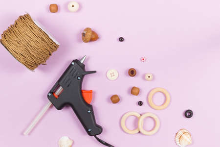 Accessories and tools for needlework, crafts, and creativity. Glue gun, wooden buttons, rings, beads, thread. Overhead, on a lilac background, a copy of the spaceの写真素材