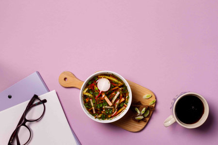 Content of the lunch break. Cold traditional Russian soup, okroshka with kvass, perfectly refreshes and quenches thirst. A bowl of soup on a wooden stand, business papers and reading glasses. Overhead, horizontal, with spaceの写真素材