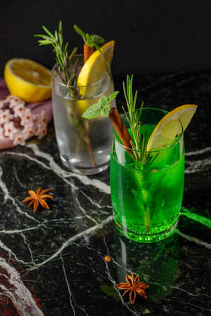 Mojito or tarragon in a steamed glass, decorated with lemon, mint and rosemary. Homemade lemonade, refreshing cocktail on a black marble background.Vertical, close-upの写真素材