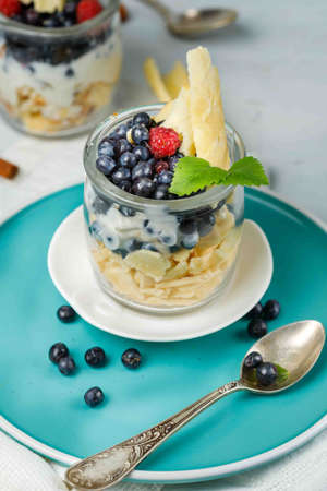 Eco dessert with blueberries, yogurt and waffle. Dessert cup on a blue plate, with a vintage spoon. Vertical frame, close-upの写真素材