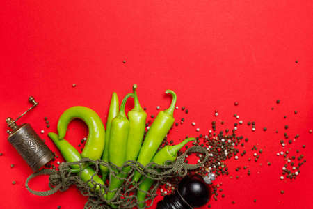 Pods of green hot pepper in a string bag,on a red background and peas of colored pepper, two spice mills on a red background, horizontal. with spaceの写真素材