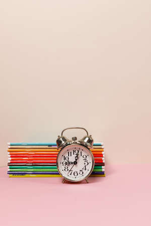 A stack of colorful notebooks and an alarm clock on the table. A vertical frame with space. Pastel...