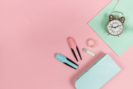 Stationery, notebooks and an alarm clock on a pink background, horizontal, with space. Top viewの写真素材