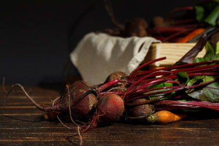 Raw beetroot with tops, on a dark wooden background and a box with vegetables in the background. Low...