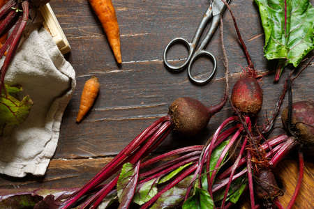 Raw beetroot with tops and carrots on a rough wooden surface. Close-up, top view, horizontal