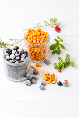 Frozen berries, sea buckthorn and aronia, in glass jars. Close-up. light, wooden light background. Vertical, selective focusの写真素材