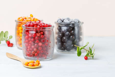 Three glass jars with frozen wild berries. Close-up, on a light background, horizontally, selective focusの写真素材