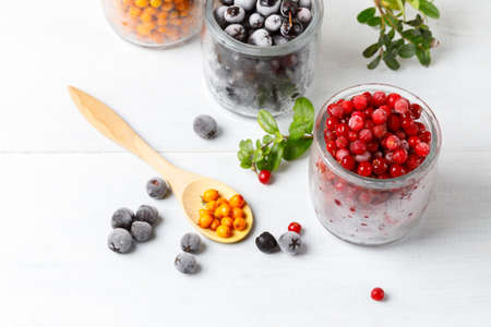 Glass jars with frozen wild berries. Close-up, on a light background, horizontally, selective focusの写真素材