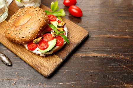 bagel with cream cheese, avocado and sweet tomatoes, on a wooden board. Wooden background, horizontal, copy of the space.の写真素材