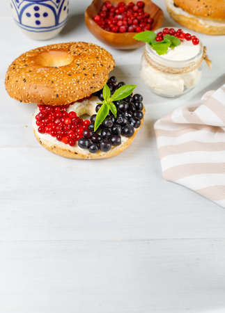 Bagel with cream cheese and fresh berries. On a light wooden background, vertical, with space. Close-upの写真素材