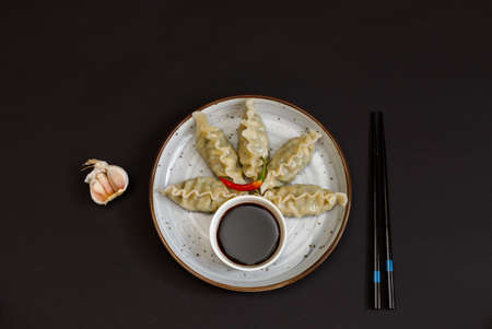 Japanese or Chinese boiled gyoza dumplings served with soy sauce. Top view on a black background, with chopsticks. With space for text. Horizontal frameの写真素材
