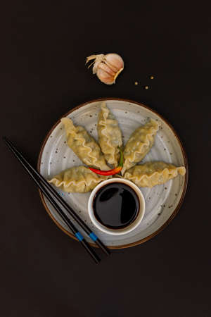 Japanese or Chinese boiled gyoza dumplings served with soy sauce. Top view on a black stone background, with chopsticks. With space for text. Vertical frameの写真素材