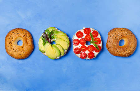 Bagels with different fillings on a blue background, top view. Bagel with tomatoes and avocado.Open sandwich with vegetable fillings Flat lay, horizontalの写真素材