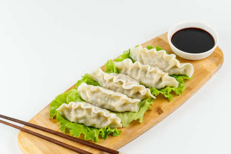 Chinese gyoza dumplings on a bamboo board with a bowl of soy sauce. Close-up on a white background.の写真素材