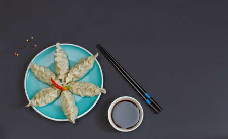 Japanese or Chinese national dish, gyoza dumplings with pork or shrimp. A portion of dumplings on a blue plate. Flatlay on a black background with chopsticks and soy sauce. Copy of the spaceの写真素材