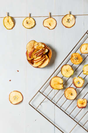 Cooking apple chips. Slices of apples on a drying rack, hung on a rope and ready chips in a bowl. Upper, vertical, light backgroundの写真素材
