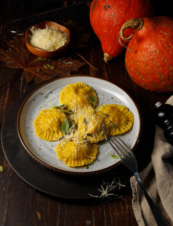 Pumpkin ravioli sprinkled with parmesan and seeds on a gray plate. Vertical frame, on a dark wooden background, with small pumpkins in the backgroundの写真素材